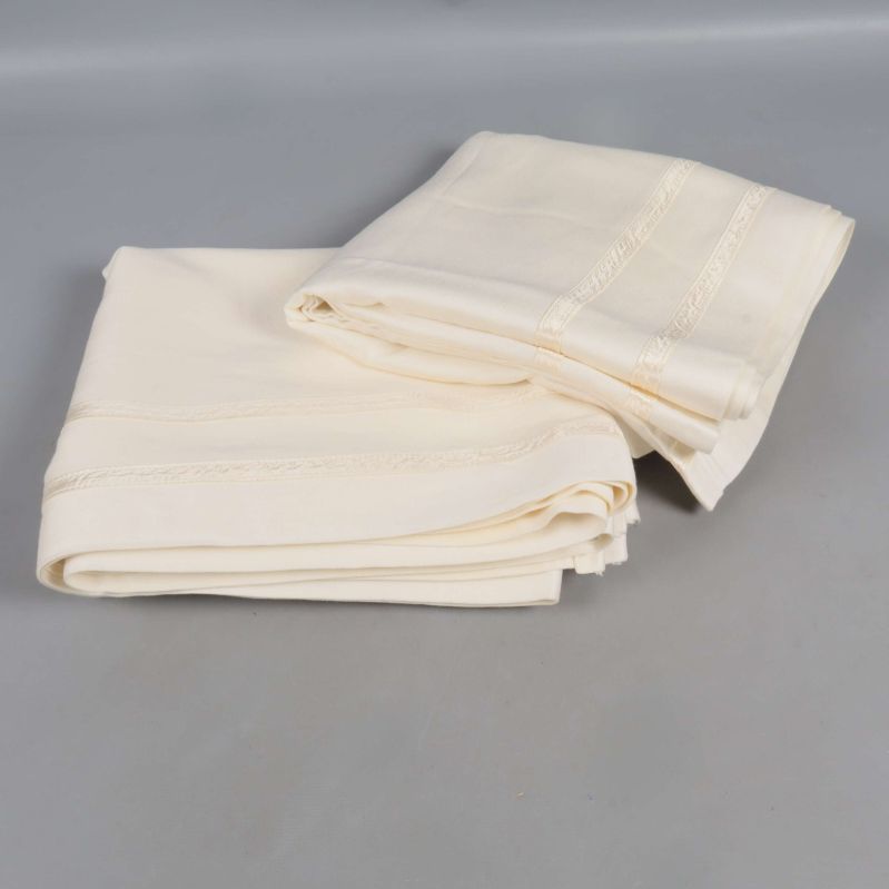 Två vikta gardinkappor i naturvit färg på grått underlag