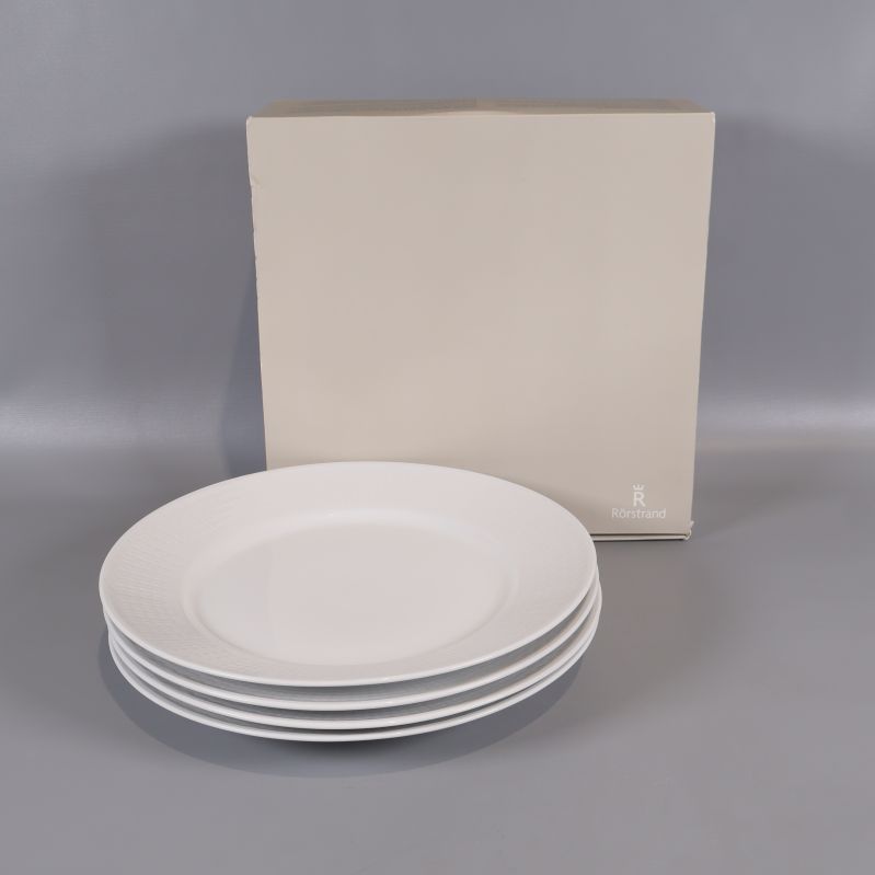 Fyra vita tallrikar framför en beige kartong