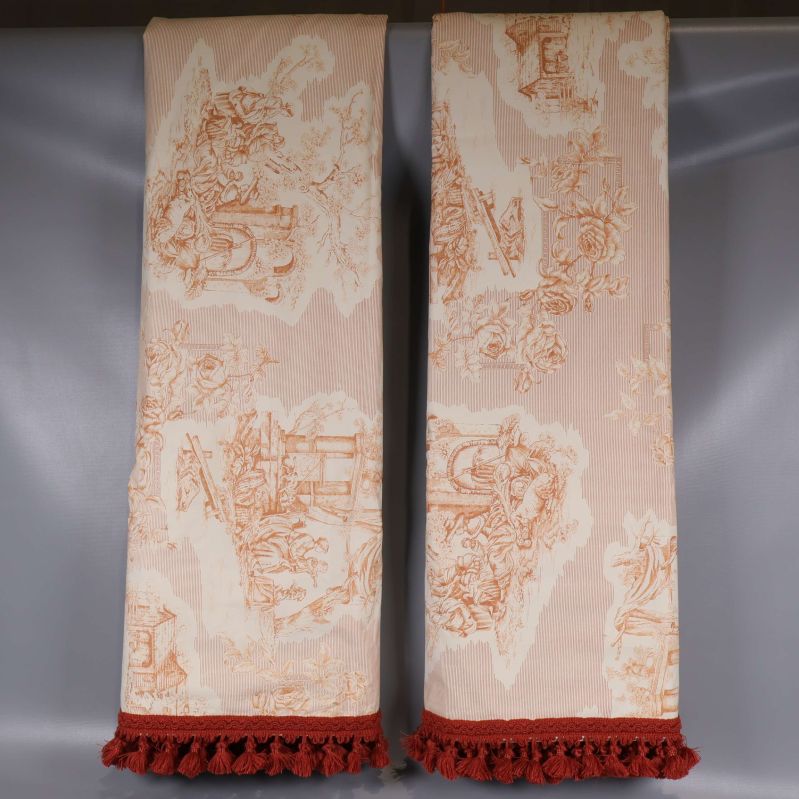 Två vikta gardinlängder med tofsar mot grå bakgrund