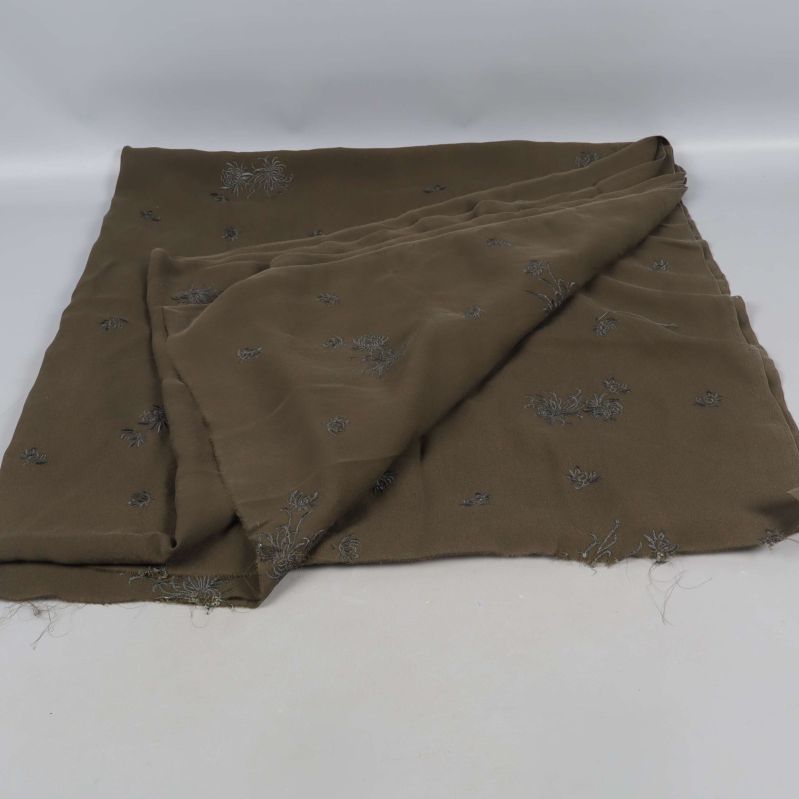 Mörk grön tyg delvis vikt ut med broderade mönster
