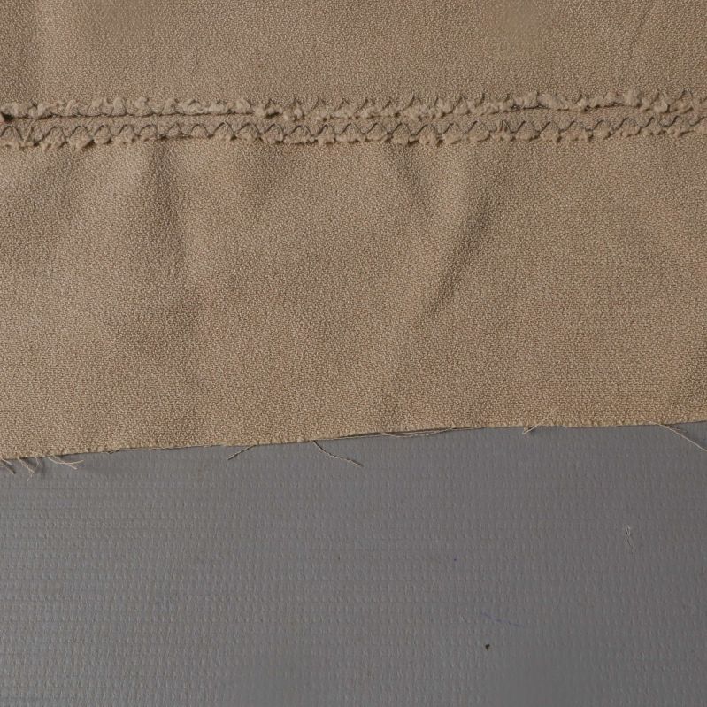 Närbild på beige tygs struktur med söm i övre delen
