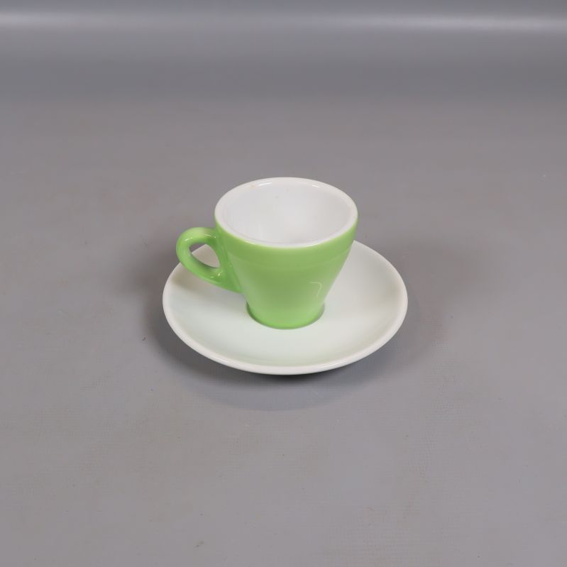 Grön espressokopp på vitt fat mot grå bakgrund