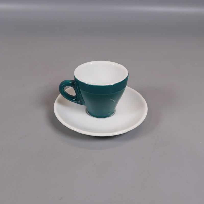 Grön espressokopp på vitt fat placerad ensam