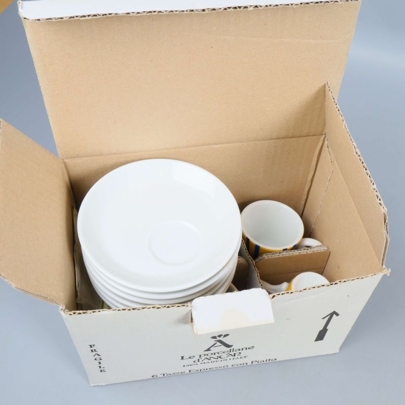 Öppen kartong som innehåller espressokoppar och fat staplade