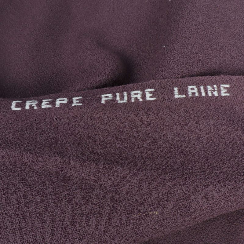 Texten CREPE PURE LAINE tryckt på lila tyg