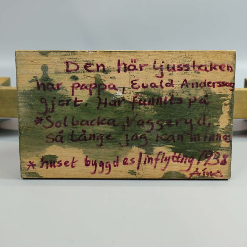 Undersidan av träljusstake med handskriven text om ursprung