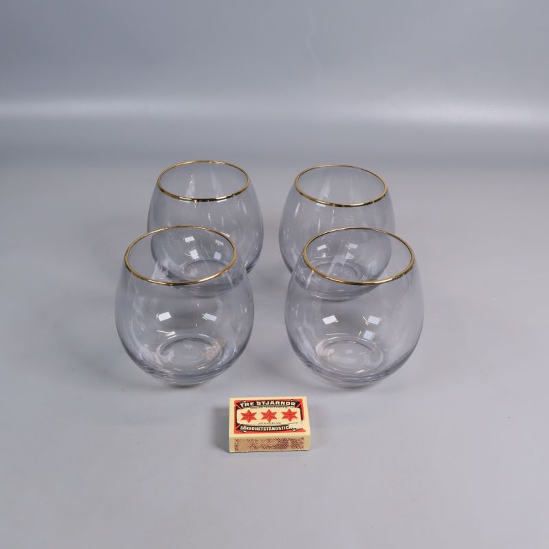 Fyra rundade glas med guldkant och tändsticksask som storleksreferens