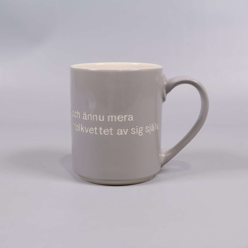 Grå mugg med vitt citat och handtag till höger