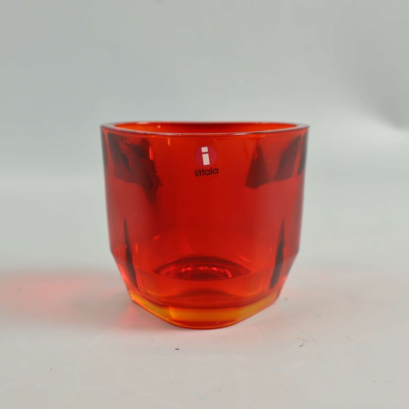Röd triangulär ljushållare i glas från Iittala mot vit bakgrund