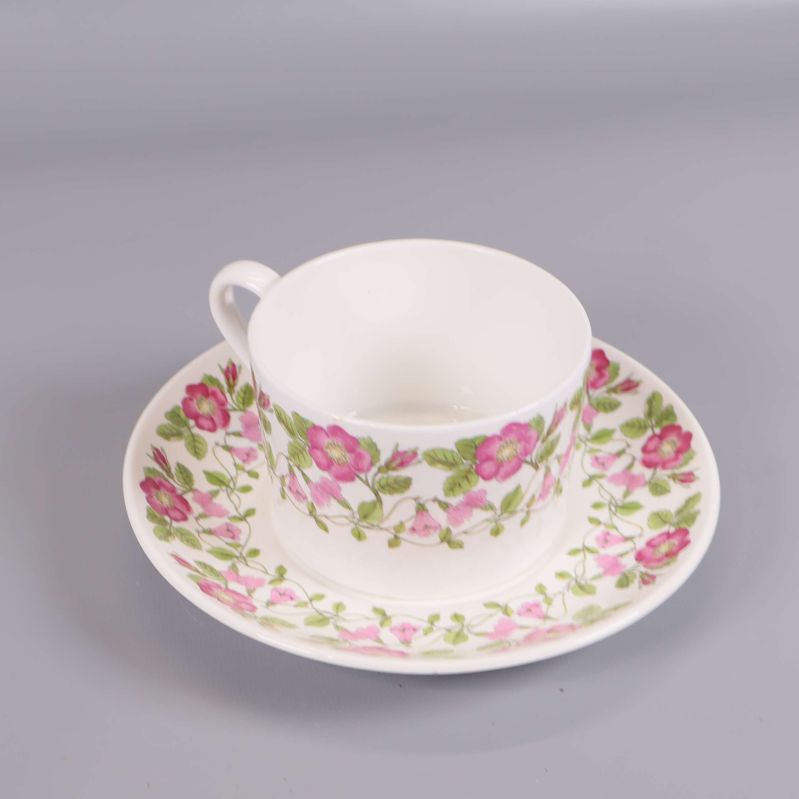 Kopp och fat med rosa och gröna blommor mot vit bakgrund