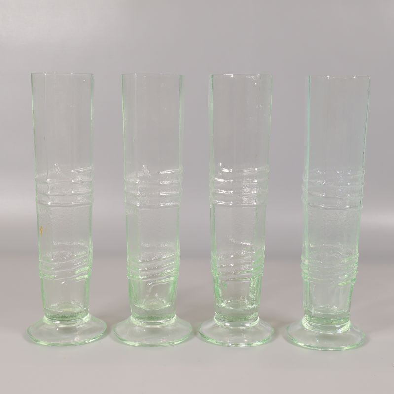 Fyra höga ljusgröna glas med räfflat mönster stående på rad