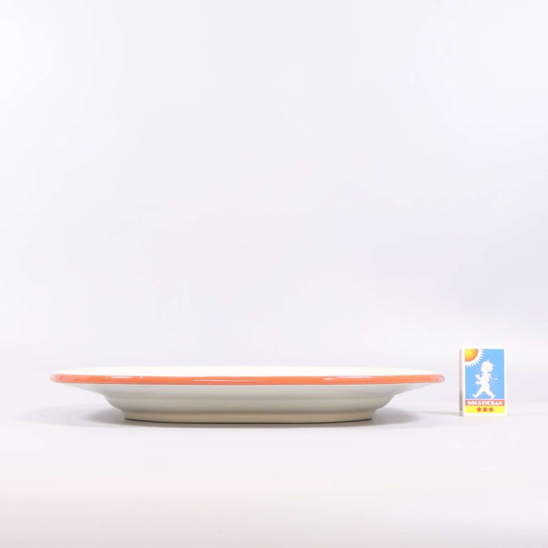 Tallrik sedd från sidan med orange kant och tändsticksask för skala