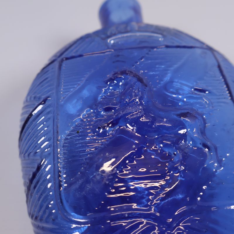 Närbild på djurrelief på mindre blå glasflaska