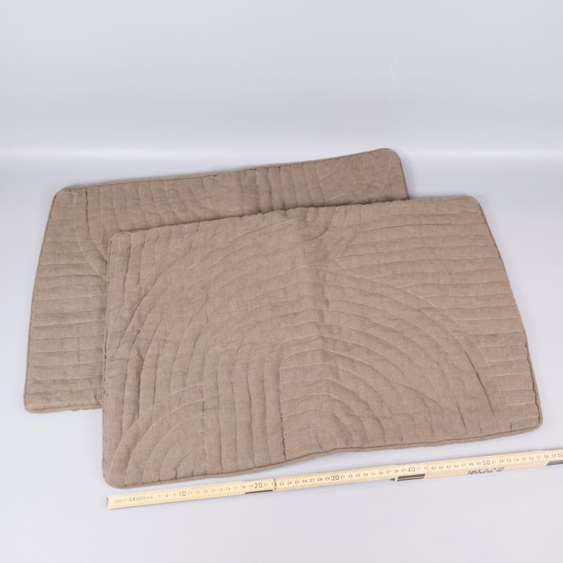 Två utlagda beige kviltade kuddfodral med måttband