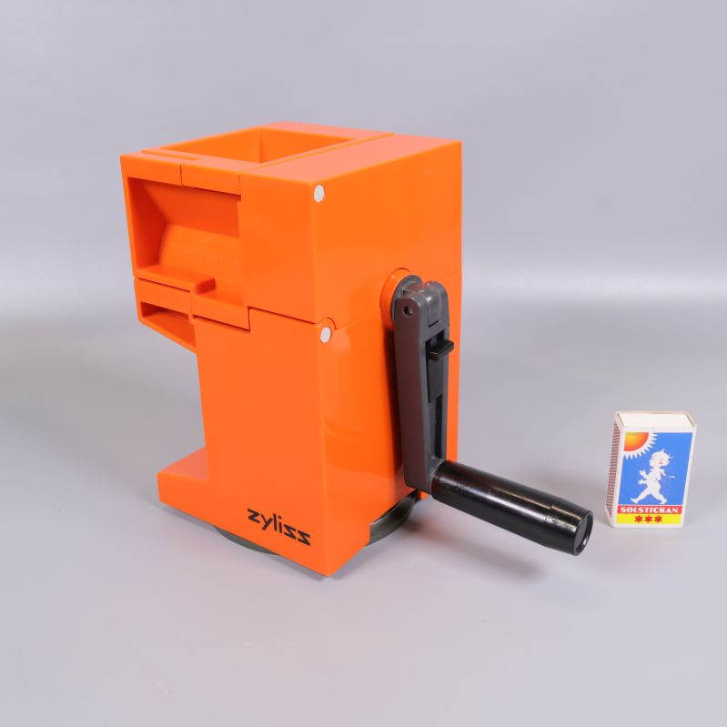 Orange grönsaksskärare från sidan med svart vev