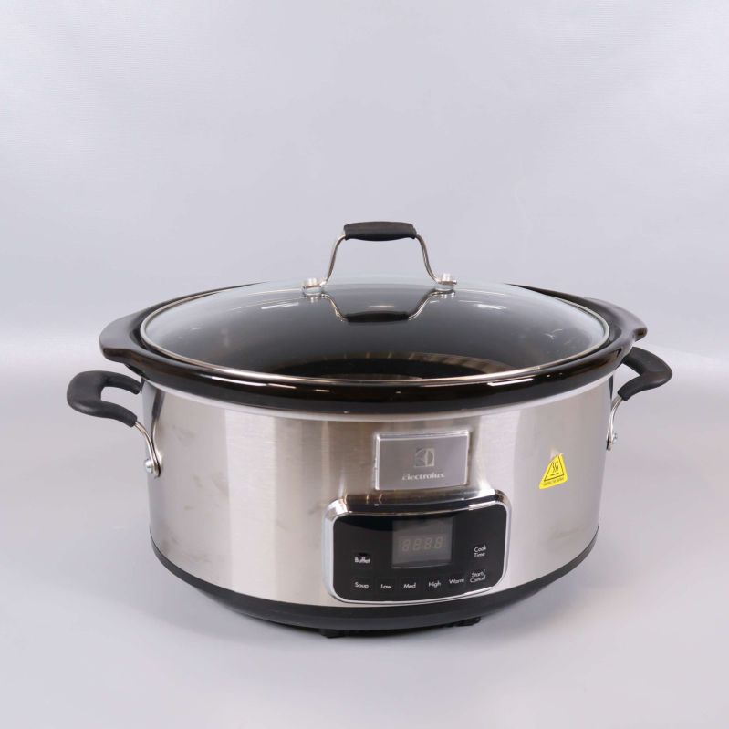 Slowcooker i rostfritt med glaslock och svarta handtag mot neutral bakgrund