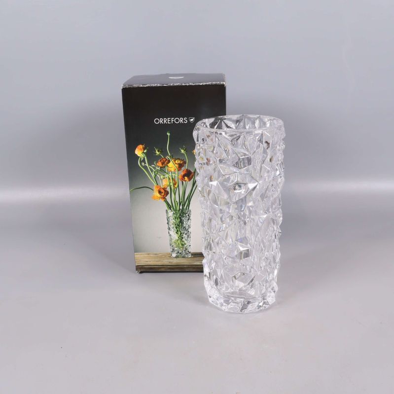 Fasetterad glasvas framför originalkartong med blommor