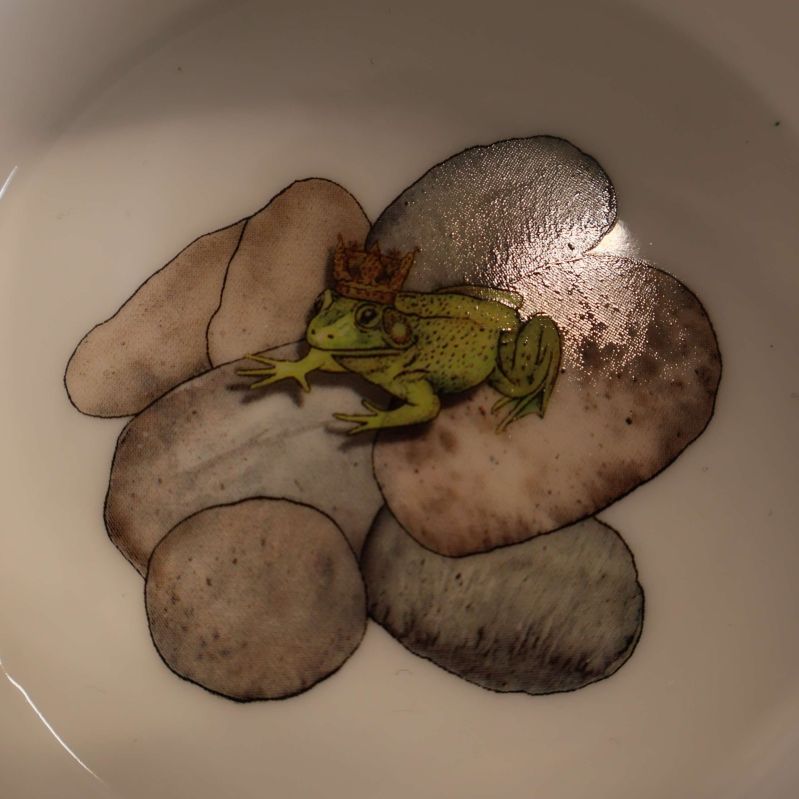 Närbild av groda med krona inuti muggens botten