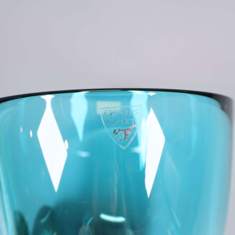 Närbild av Orrefors-logotyp på blå glasskål