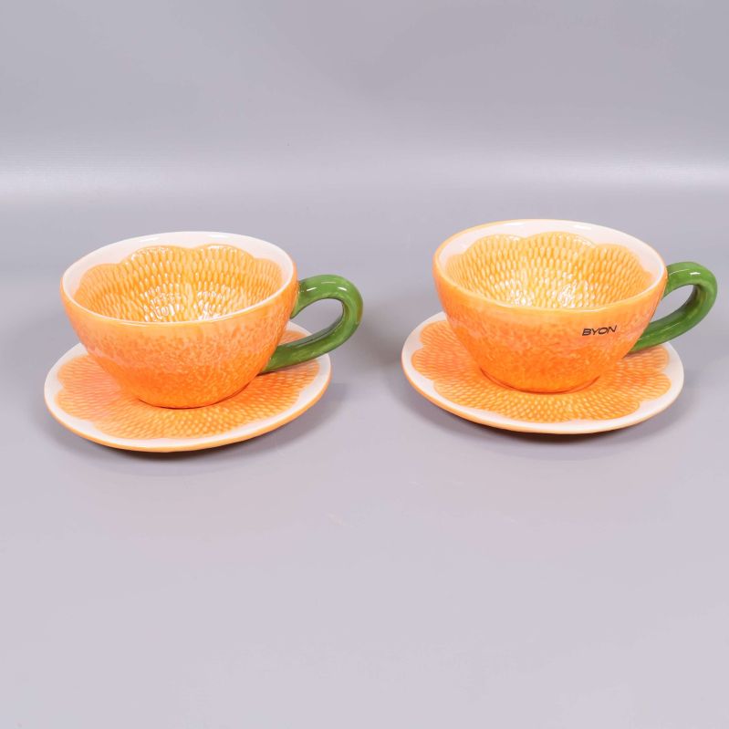Två koppar med orange mönster och gröna handtag på fat