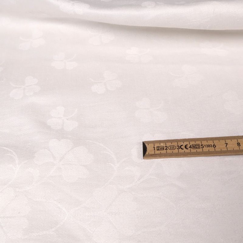 Närbild på vävt klövermönster i vit textil med linjal