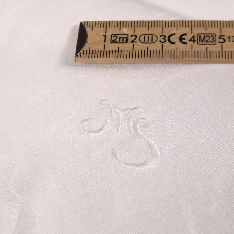 Närbild på vitt broderat monogram och måttstock