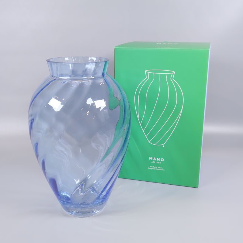 Blå glasvas med spiraldesign bredvid grön förpackning