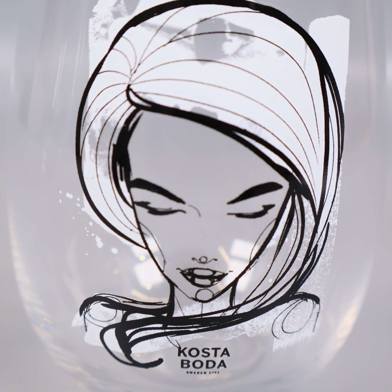 Närbild av glas med tecknat ansikte och Kosta Boda-logotyp