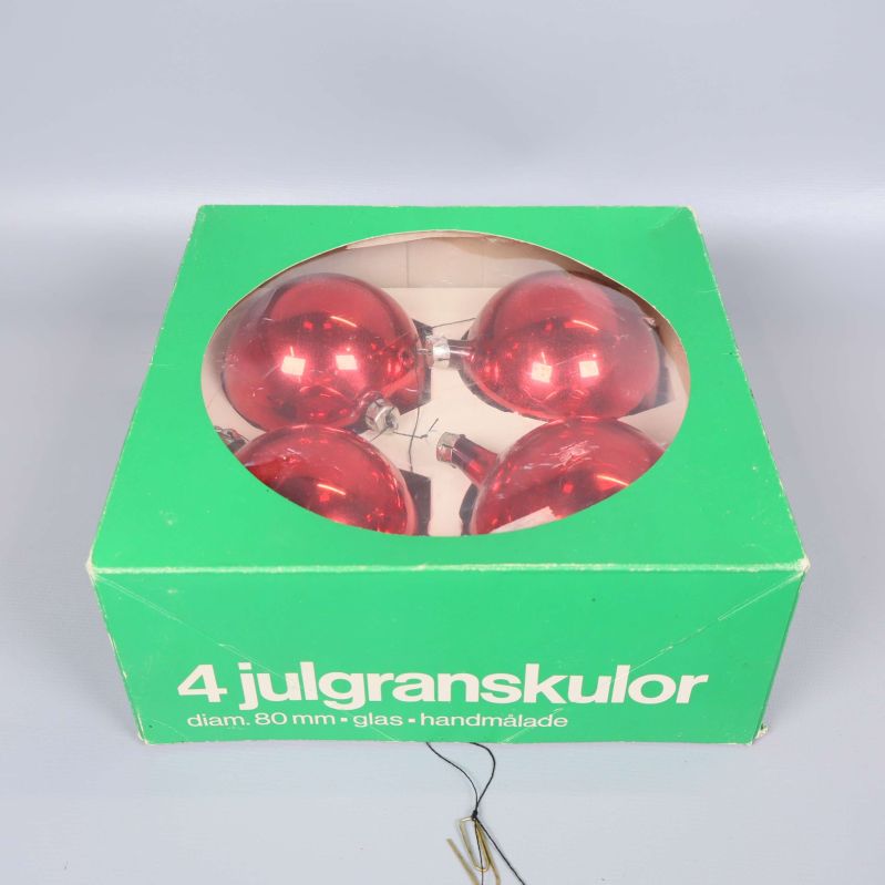 Fyra röda julgranskulor ligger i en grön förpackning