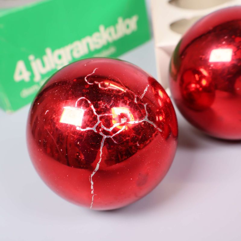 Julgranskula i rött med flera sprickor, förpackning i bakgrunden