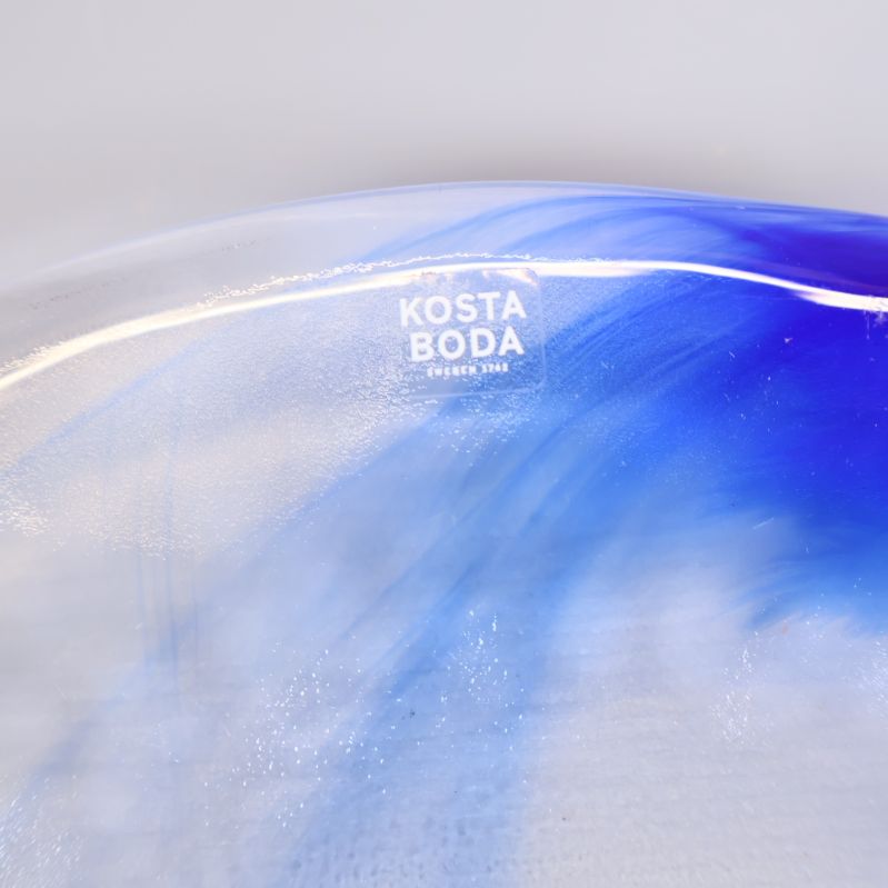Kosta Boda-logga på blått glasfat i närbild
