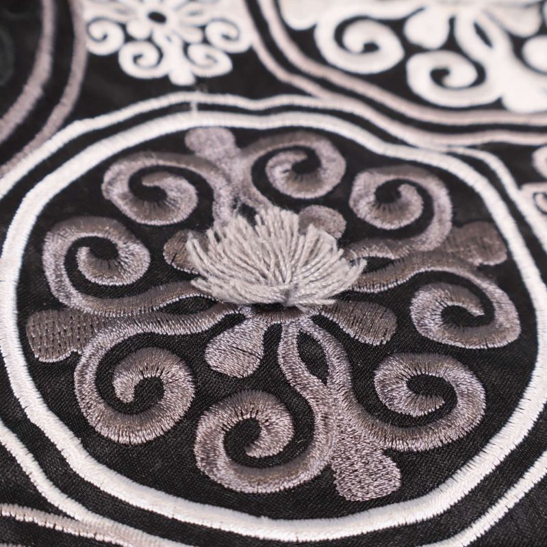 Närbild av grå broderad blomdetalj på svart ornamentmönster