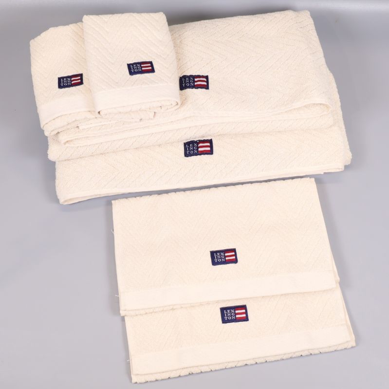 Flera naturvita Lexington-handdukar vikta i olika storlekar på grå bakgrund
