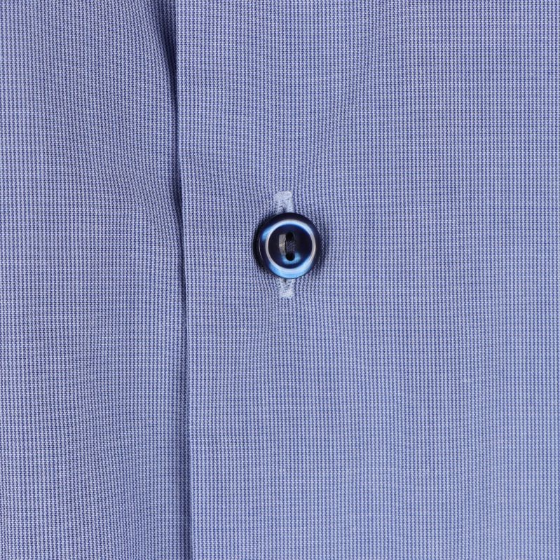 Närbild på skjortknapp på ljusblå tyg