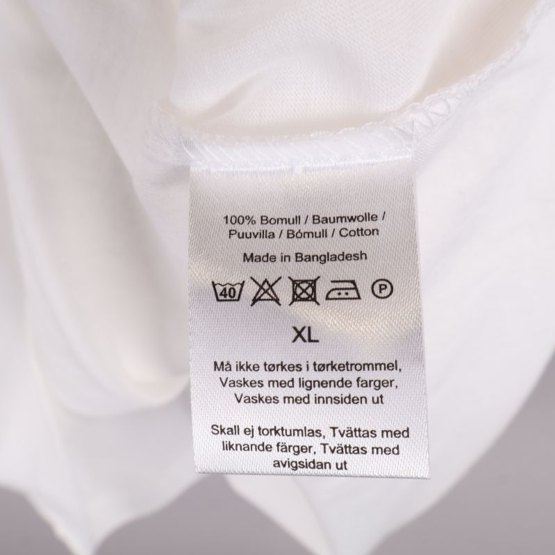 Tvättetikett på vit t-shirt visar material och skötselråd