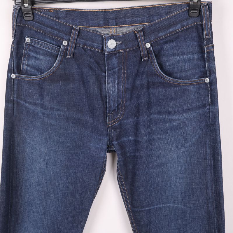 Närbild framtill med fickor och midjeknappar på blå jeans