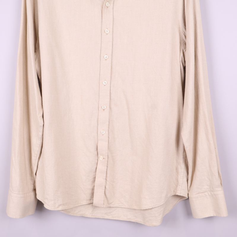 Nedre delen av beige skjorta med knappslå och rundad fåll