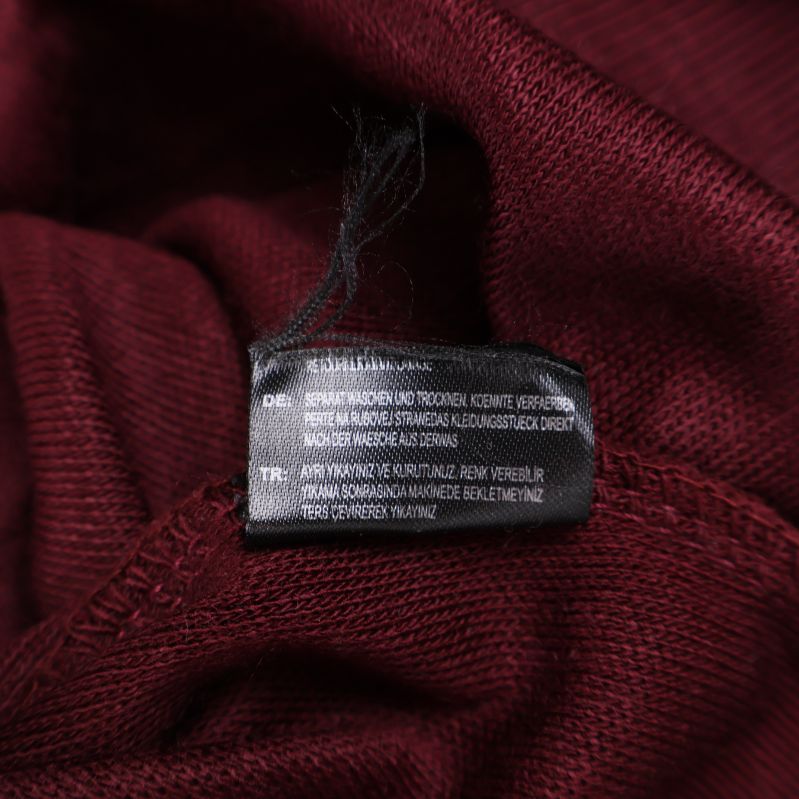 Närbild av materiallapp i vinröd tröja med tvättråd och materialinfo