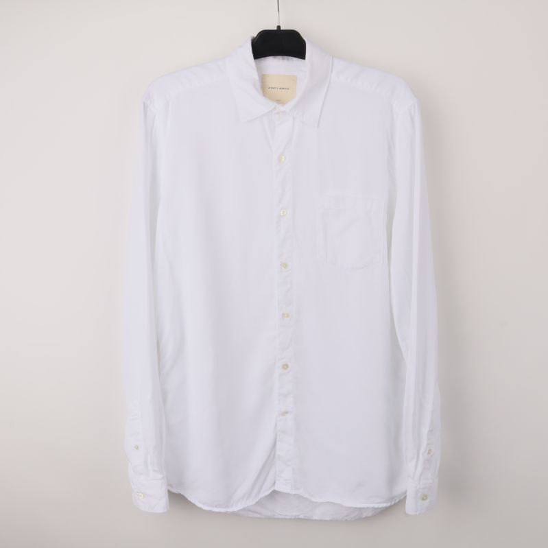 Vit långärmad skjorta på galge mot ljus bakgrund