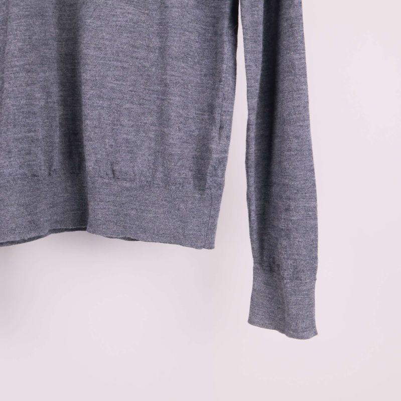 Närbild på nederkant och ärm av grå stickad tröja