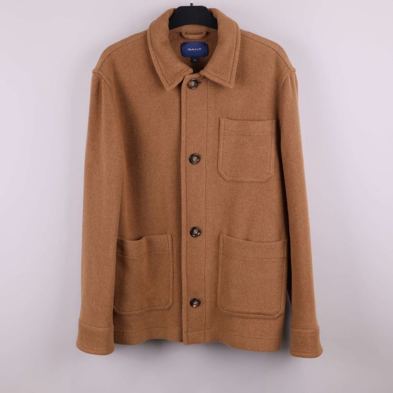 Beige kavaj med knappar och stora utanpåfickor hängande på galge