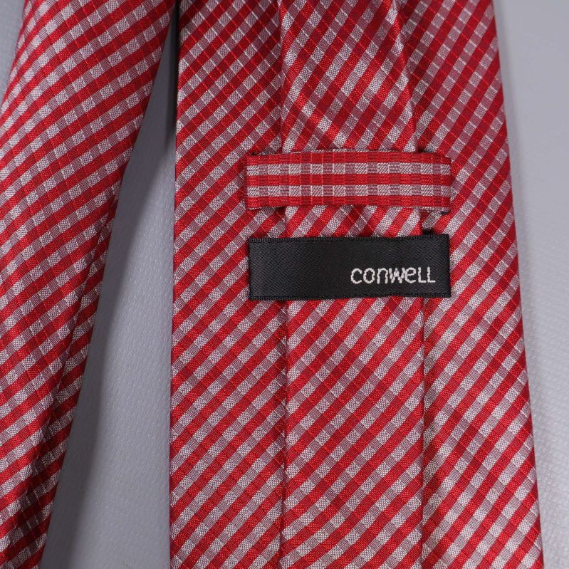 Närbild av etikett med texten Cornwell på rödvit slips