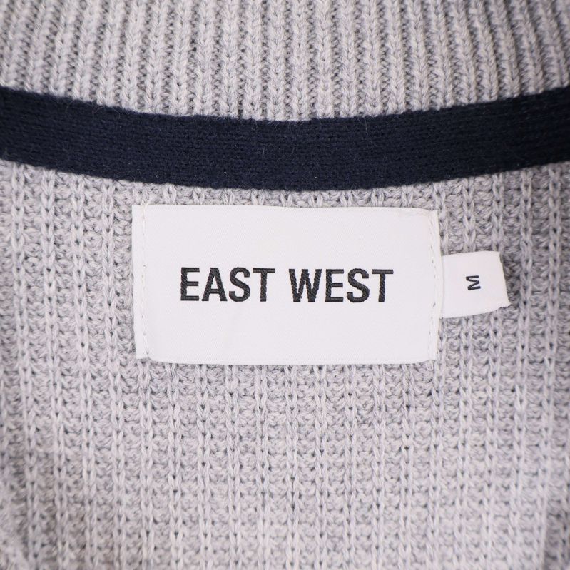 Närbild på etikett med EAST WEST och storlek M