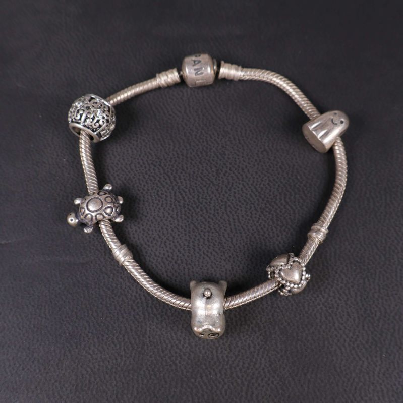 Silverfärgat armband med fem olika berlocker liggande på mörk yta