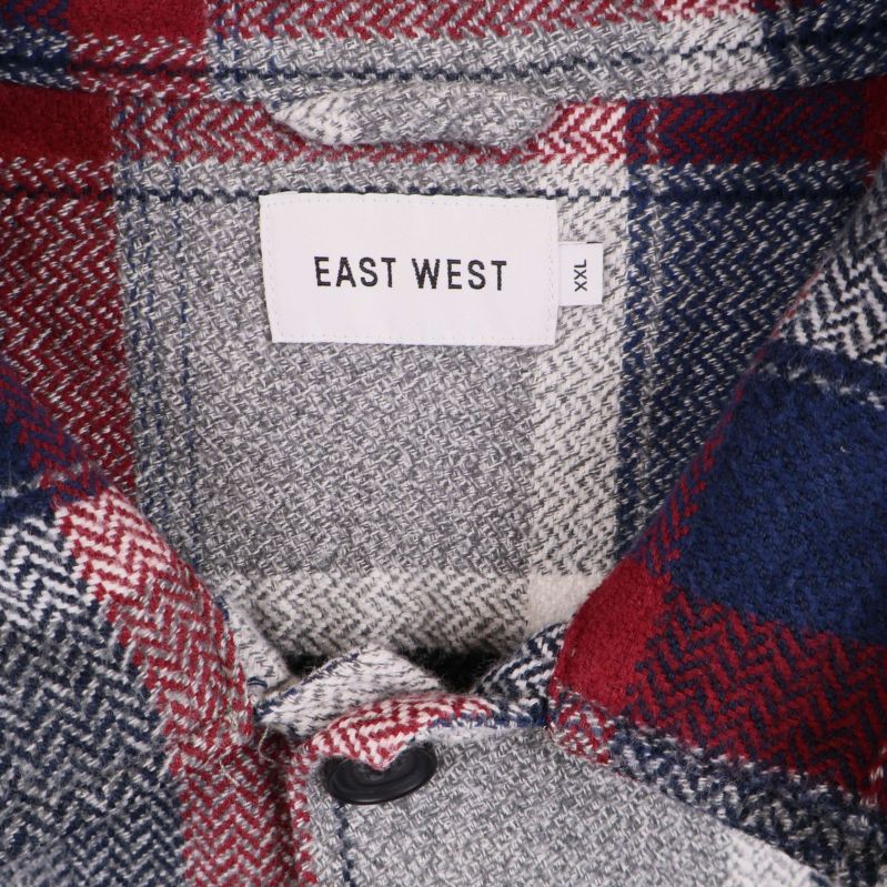 Närbild på etikett med texten East West XS i skjortan