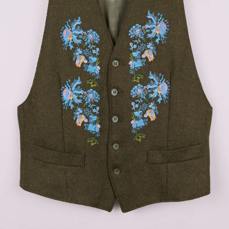 Närbild på broderier och knappar framtill på väst