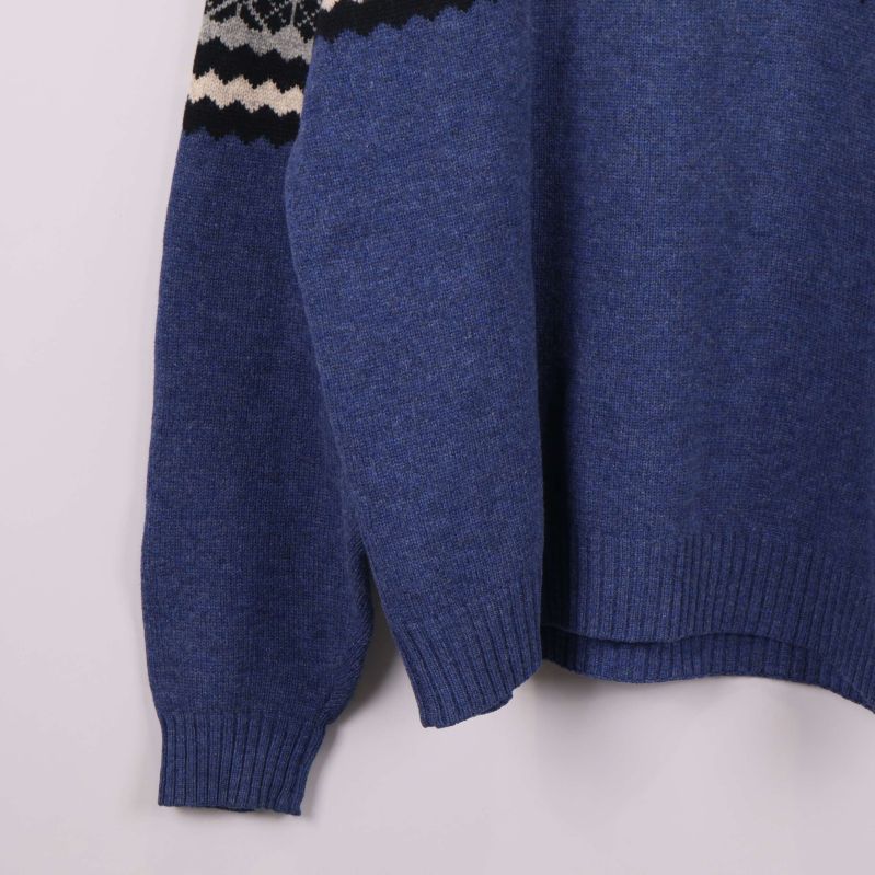 Närbild på ärm och nederkant på blå stickad tröja med ribbad mudd