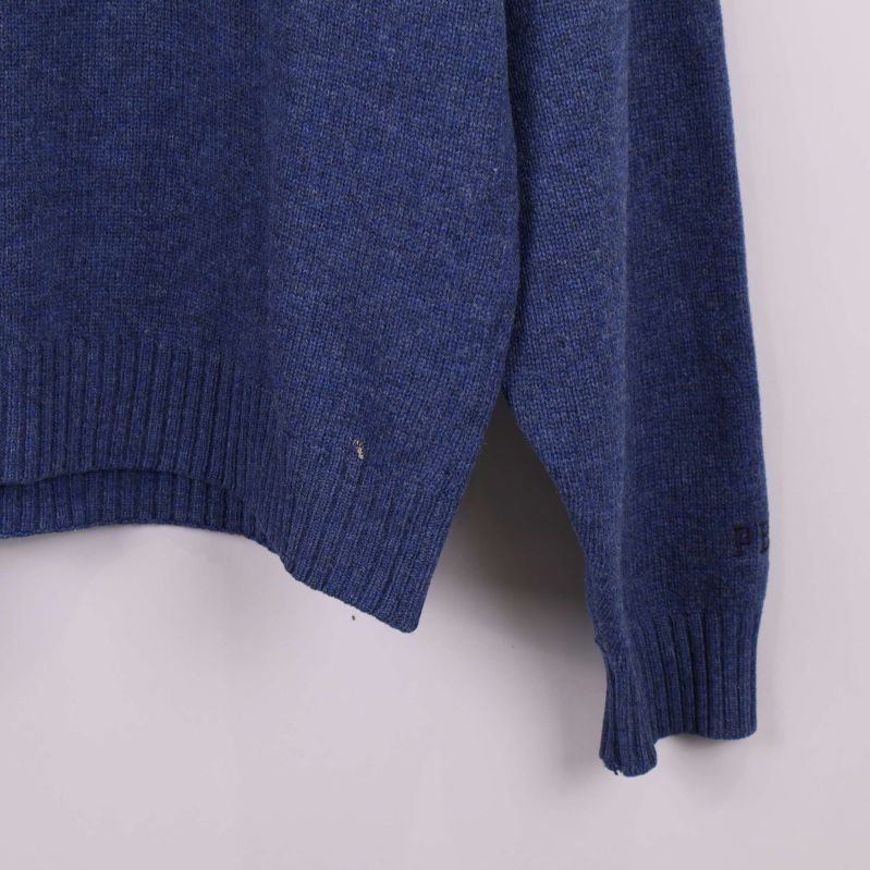 Närbild på nederkant med liten skada på blå stickad tröja