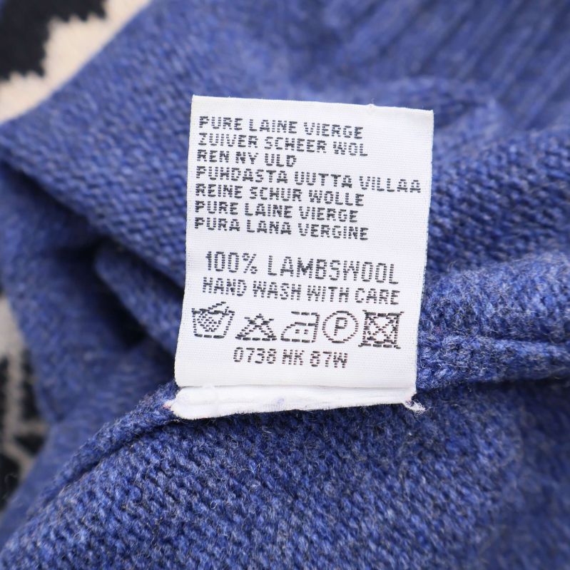 Materiallapp som visar 100% lammull på blå stickad tröja