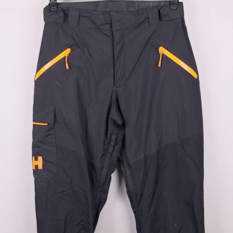 Fickor och orange dragkedjor på svarta byxors framsida